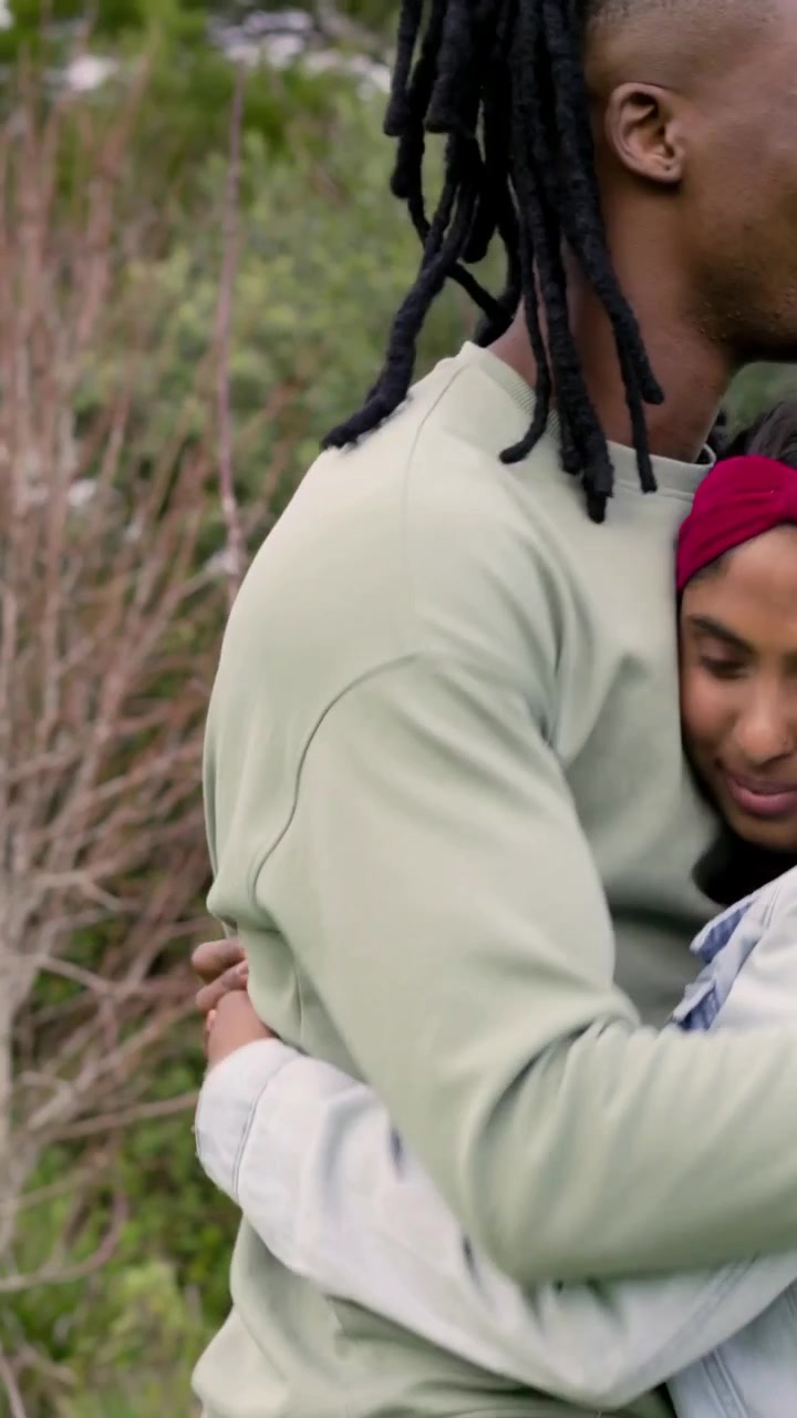 Vertical video: Hugging couple holding for comfort in park while camera pans right showing jacket