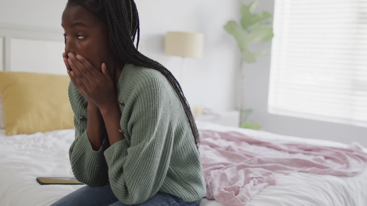 Adolescente afro-americana triste sentada na cama cobrindo o rosto.