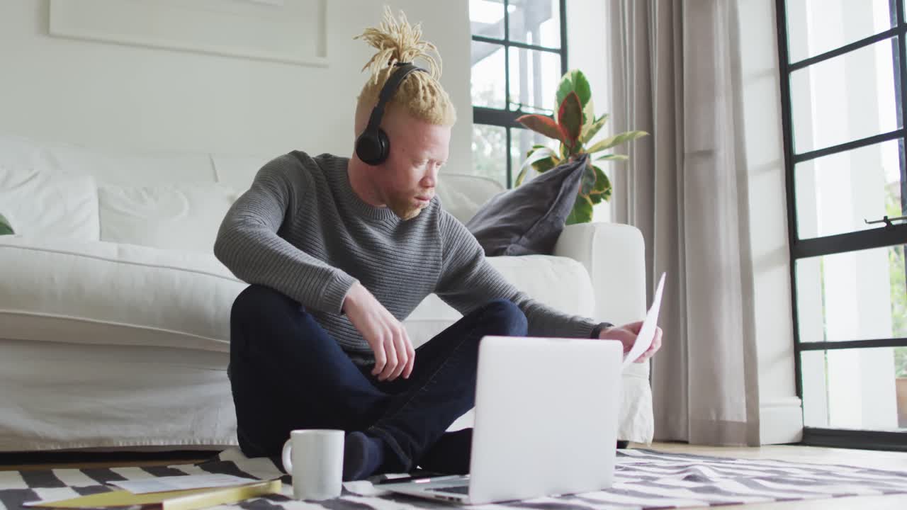 Albino african american man with dreadlocks siting on the floor, working and using laptop