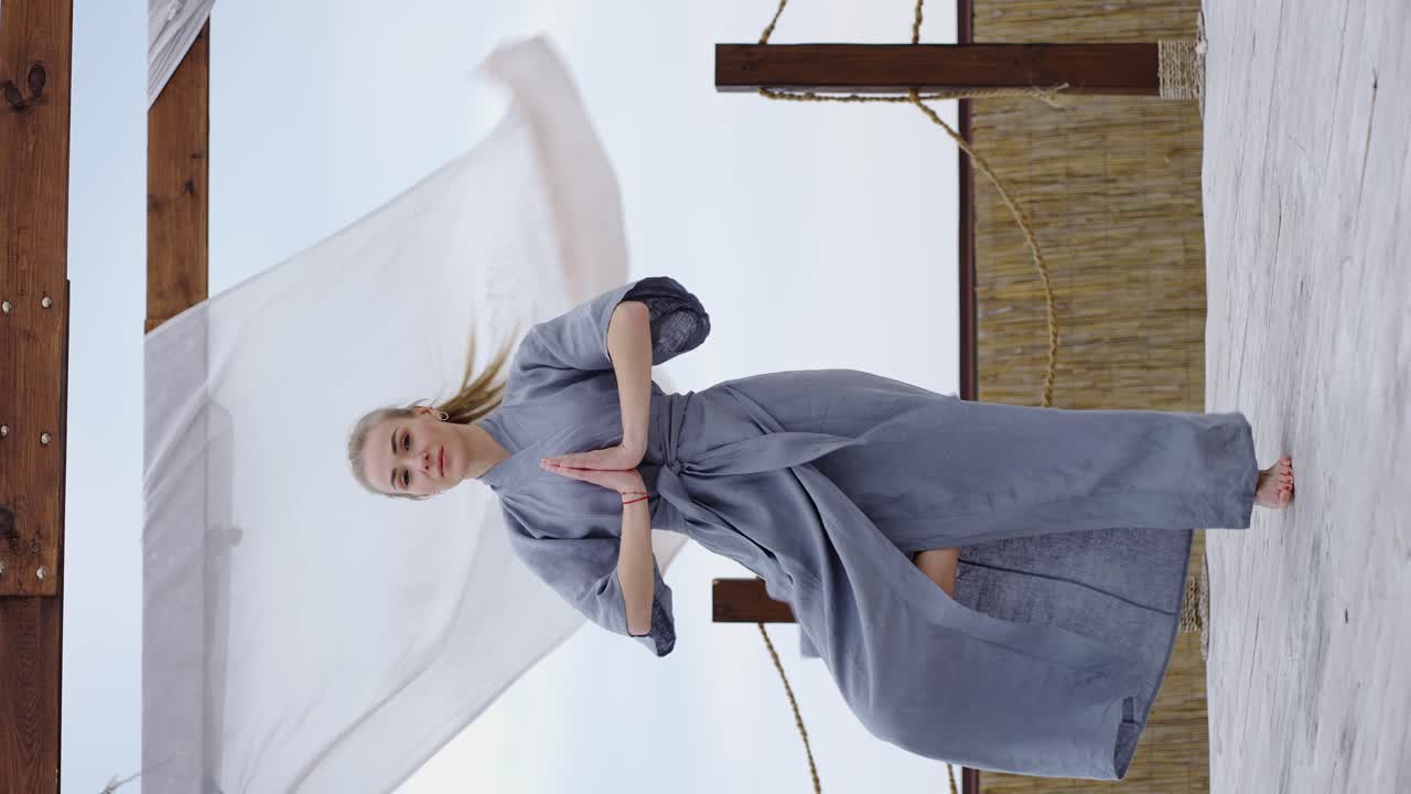 테라스 에서 파란 옷 을 입은 금발 여자 가 나마스테 에서 요가 포즈 를 취 하고 있다