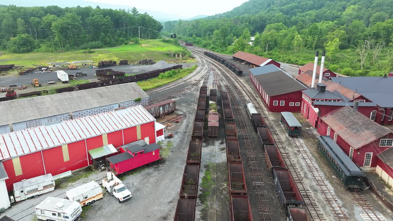 This location features a vast, abandoned train yard with rusty train cars and historic industrial buildings. Surrounded by lush green mountains, it showcases a piece of transportation history