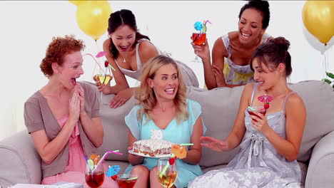 woman blowing out the birthday candles surrounded by her friends