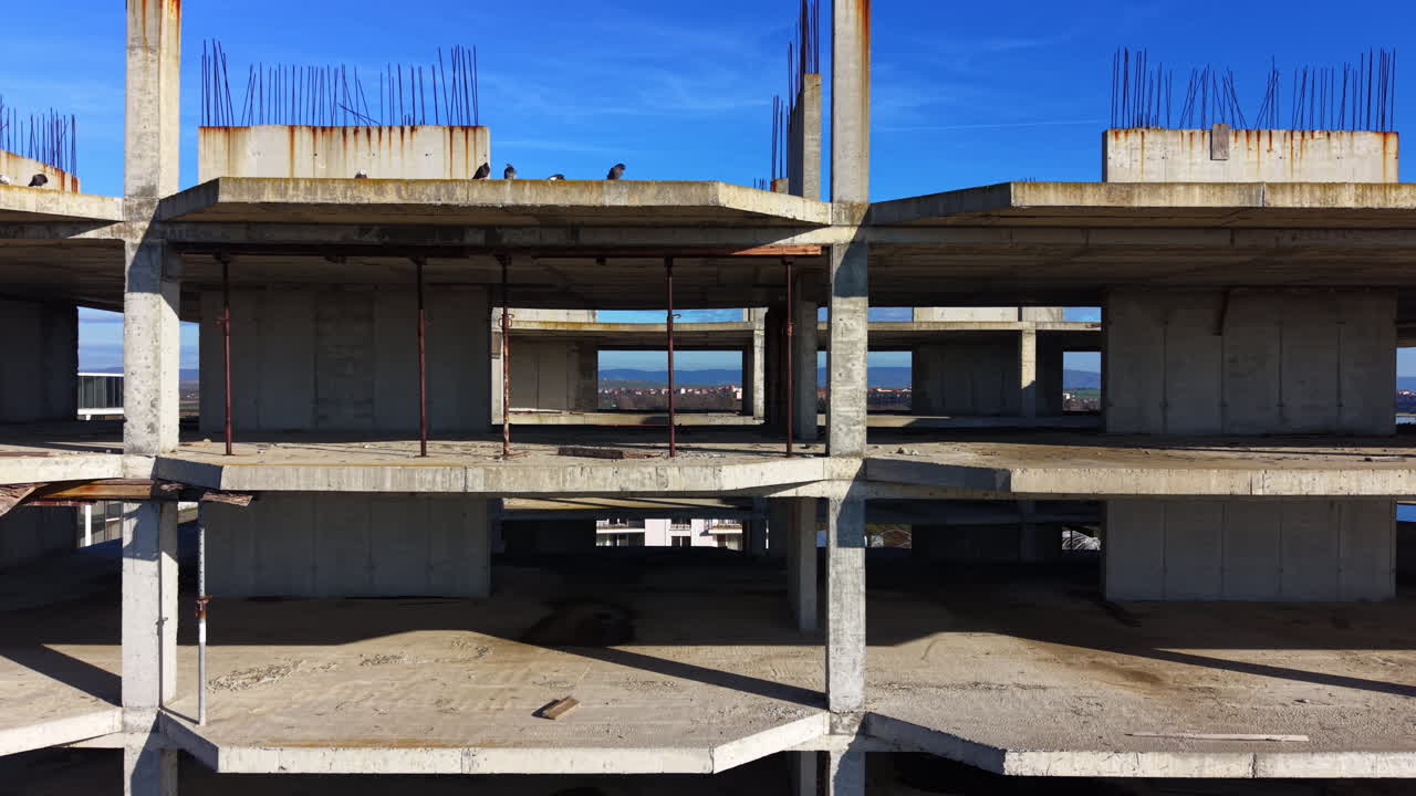Gebouw met meerdere verdiepingen met zichtbare wapening en vogels op de bovenste verdieping. Verlaten betonconstructie met roestvlekken. Luchtfoto