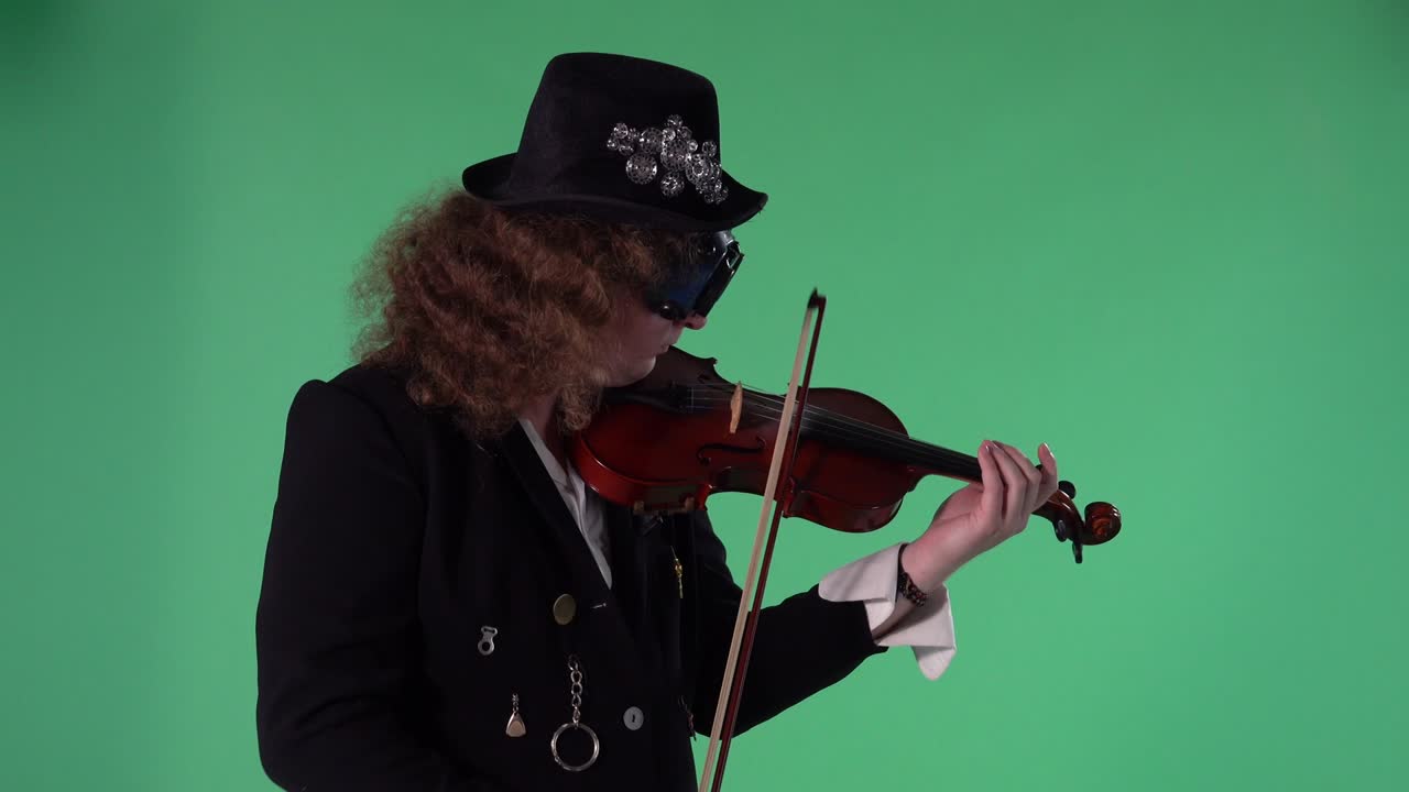 un violinista con un traje negro, sombrero y gafas originales toca el violín con maestría. el hombre toca las cuerdas con un arco para crear una melodía. pantalla verde clave de croma. vista lateral. cámara lenta.