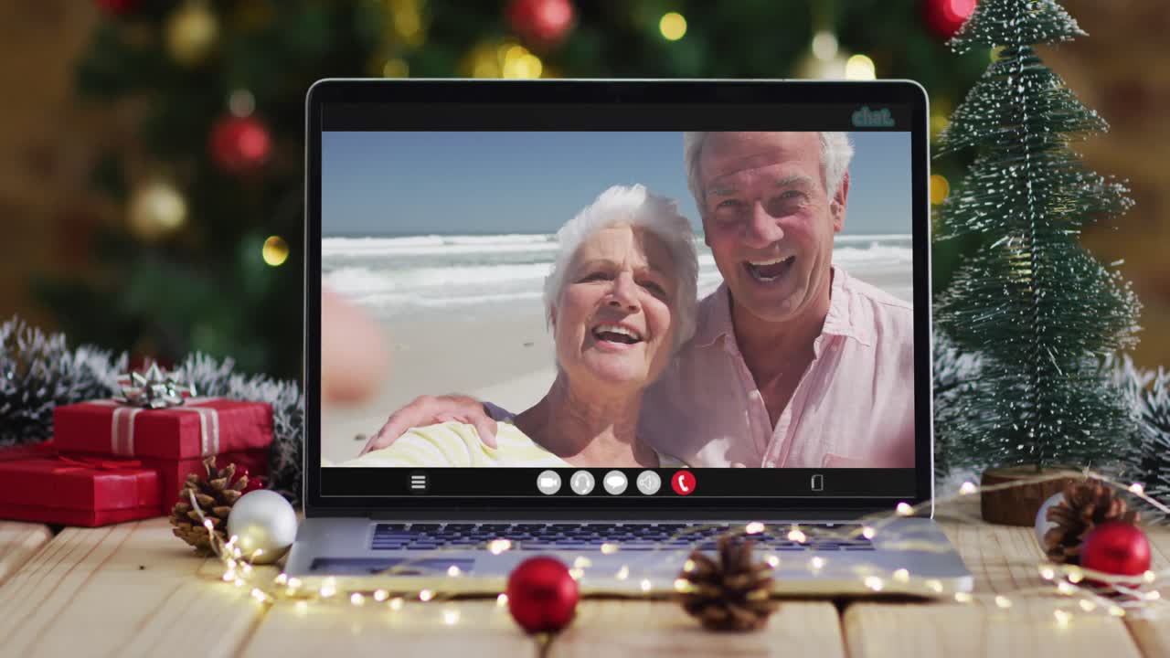 una pareja de alto nivel caucásica saludando en una videollamada en una computadora portátil, con un árbol de navidad