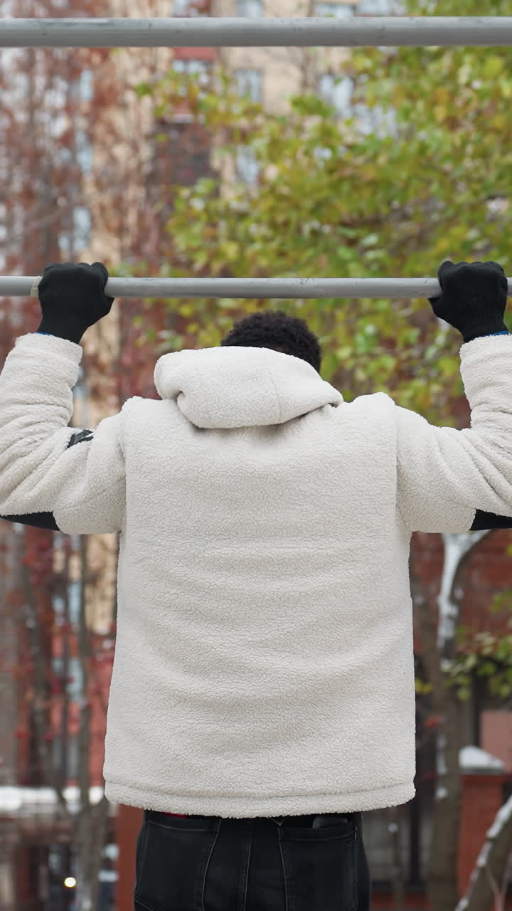 색 겨울 재을 입은 어린 소년이 야외 운동 장비를 잡기 위해 점프하고, 도시 환경에서 당겨서 즉시 내려가는 후면 모습