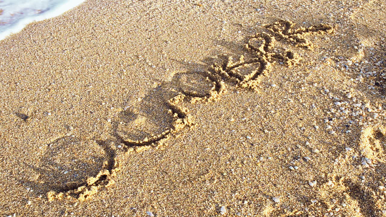 Inscription October on sand. The inscription is washed away by a sea wave. Shooting on the beach