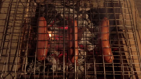 birds eye shot of sausages on a charcoal bbq at night creating flames - smoke from the dripping fat