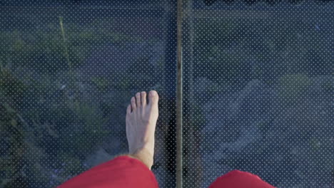 bare feet walking over glass deck with large drop underneath, slow motion