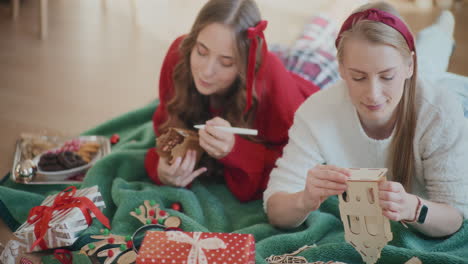 young sisters making cardboard house ornaments during christmas at home