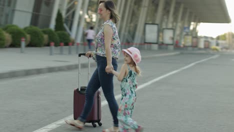 mother and daughter walking outdoors to airport. woman carrying suitcase bag. child and mom vacation