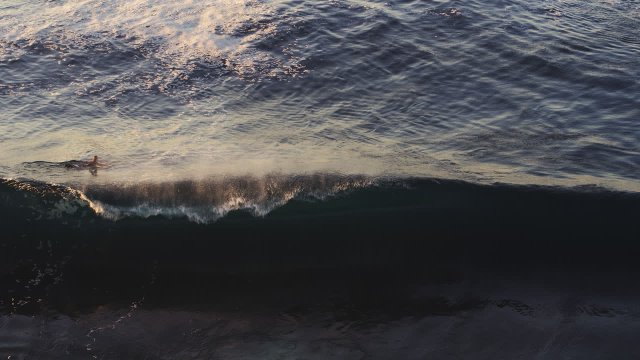 Aerial top shot of powerful ocean wave crashing and glistening with golden sunlight