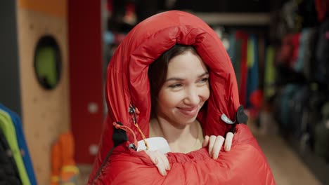 a smiling woman purchase in sportswear store, checking and trying sleeping bag in front camera