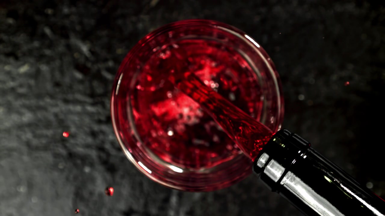 Vino rosso versato dalla bottiglia nel bicchiere al rallentatore, vista dall'alto.