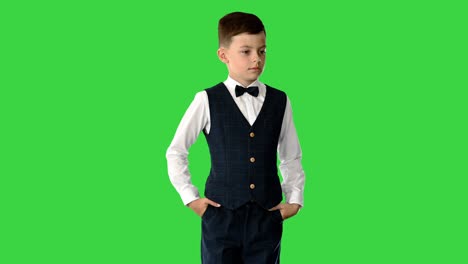 young boy in bow tie and suit holding hands in pockets with his eyes down on a green screen, chroma key