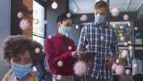 covid-19 cells against male and female office colleagues wearing face masks discussing at office