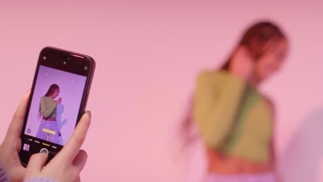 분홍색 배경에 휴대 전화로 춤추는 친구의 사진을 찍는 여성의 스튜디오  3
