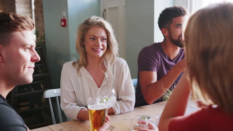 vista de cerca de cuatro colegas adultos jóvenes sentados en una mesa, bebiendo y hablando en un pub