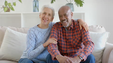 Portrait-of-happy-senior-biracial-couple-sitting-on-couch-embracing-and-talking-at-home,-slow-motion