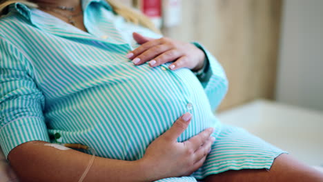 expecting mother strokes her big belly. drop counter is connected to female hand. close up. maternity hospital patient before childbirth.