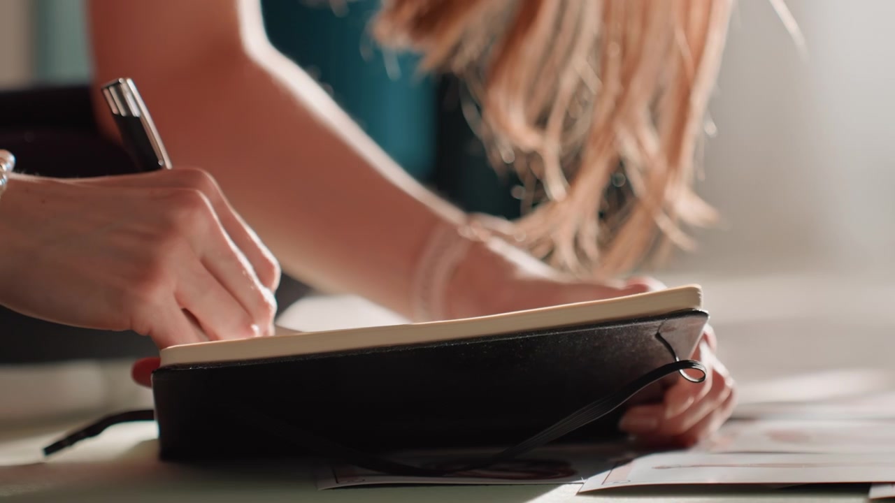 Donna caucasica che scrive un diario di fitness su un tappetino, quaderno nero e braccialetto di perle sotto la calda luce del sole, tratti di penna che segnano il piano di allenamento, pavimento accogliente del soggiorno, mani in primo piano che creano la routine settimanale