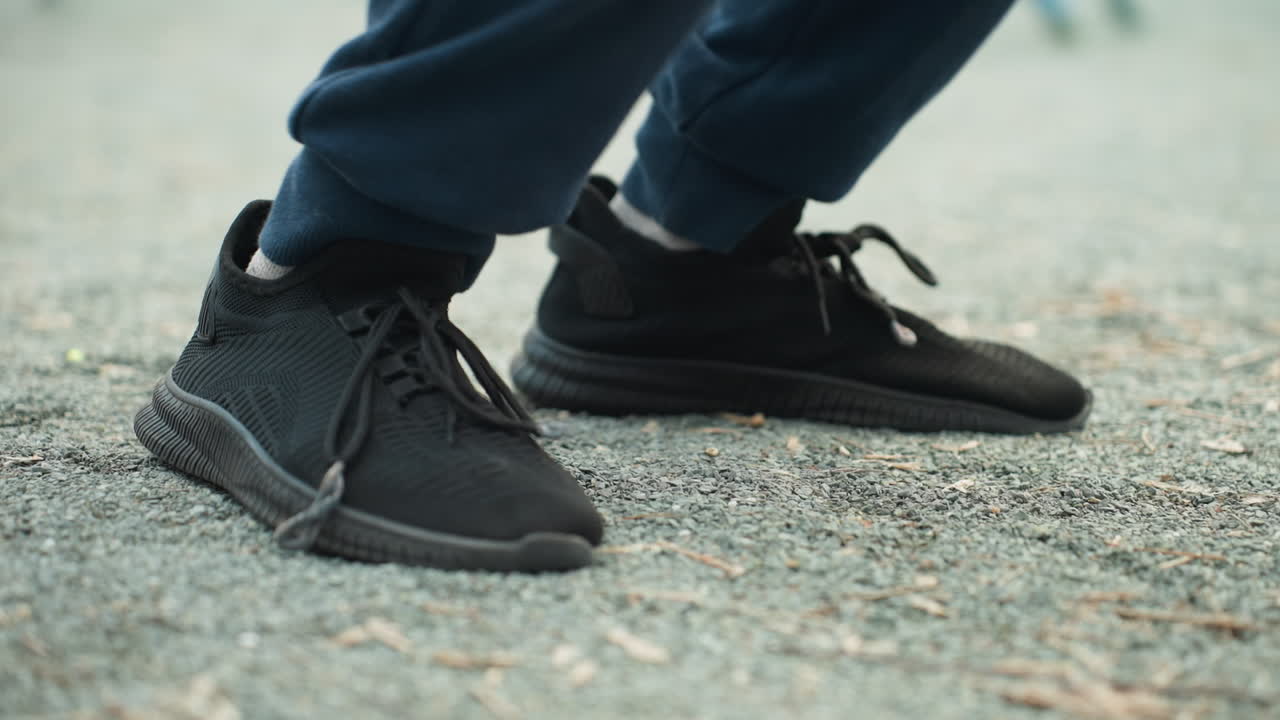 Close-up view of someone in black sneakers and blue trousers moving their leg forward and backward with a blurred background