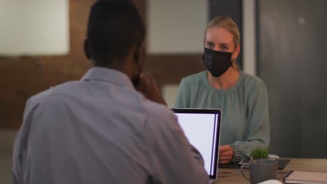 diverse male and female business colleagues wearing masks in discussion at work