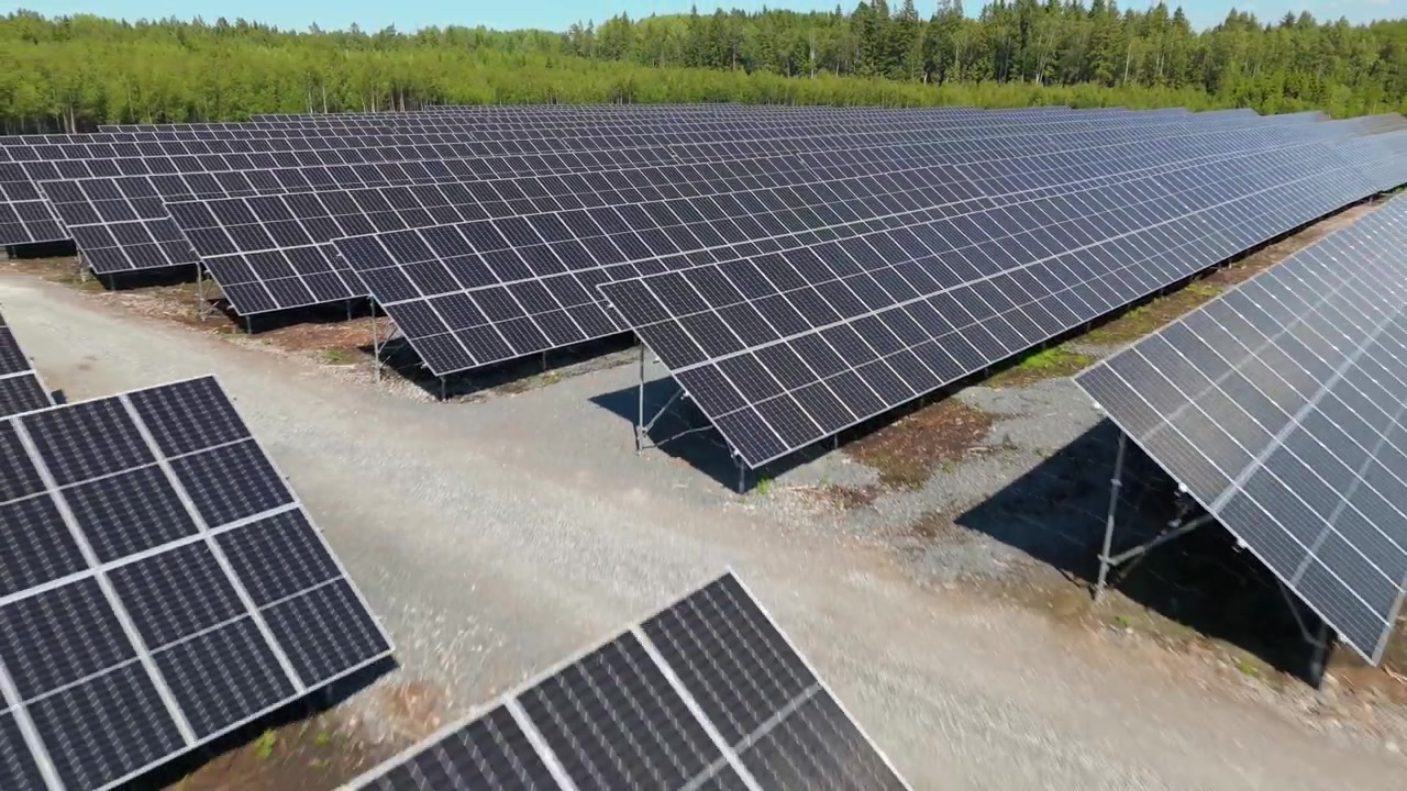 Rapido pullback aereo a bassa quota sopra pannelli solari bifacciali in un parco solare in Finlandia, produzione di energia con ghiaia tra le file