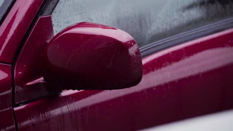 wet side-view mirror of red car. closeup shot