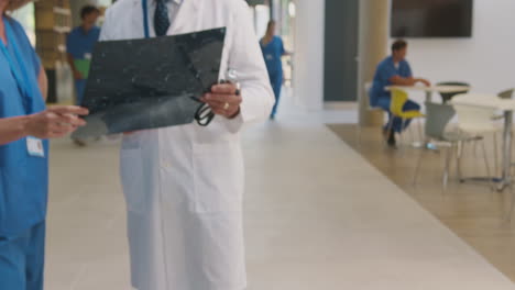 doctor wearing white coat discussing patient scan with female colleague in busy hospital