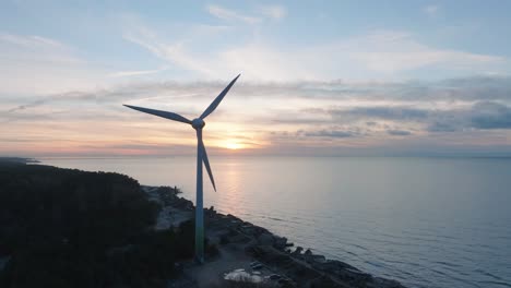 Aerial-establishing-view-of-abandoned-seaside-fortification-buildings-at-Karosta-Northern-Forts-on-the-beach-of-Baltic-sea-in-Liepaja,-sunset,-golden-hour,-wind-turbine,-wide-drone-shot-moving-forward
