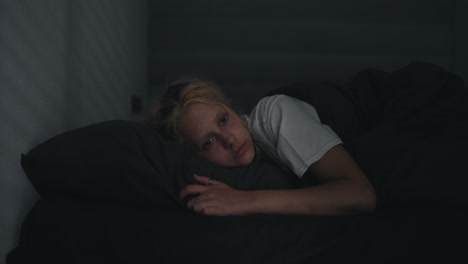 A-young-blonde-girl-in-a-white-T-shirt-wakes-up-abruptly-while-lying-in-a-serious-bed