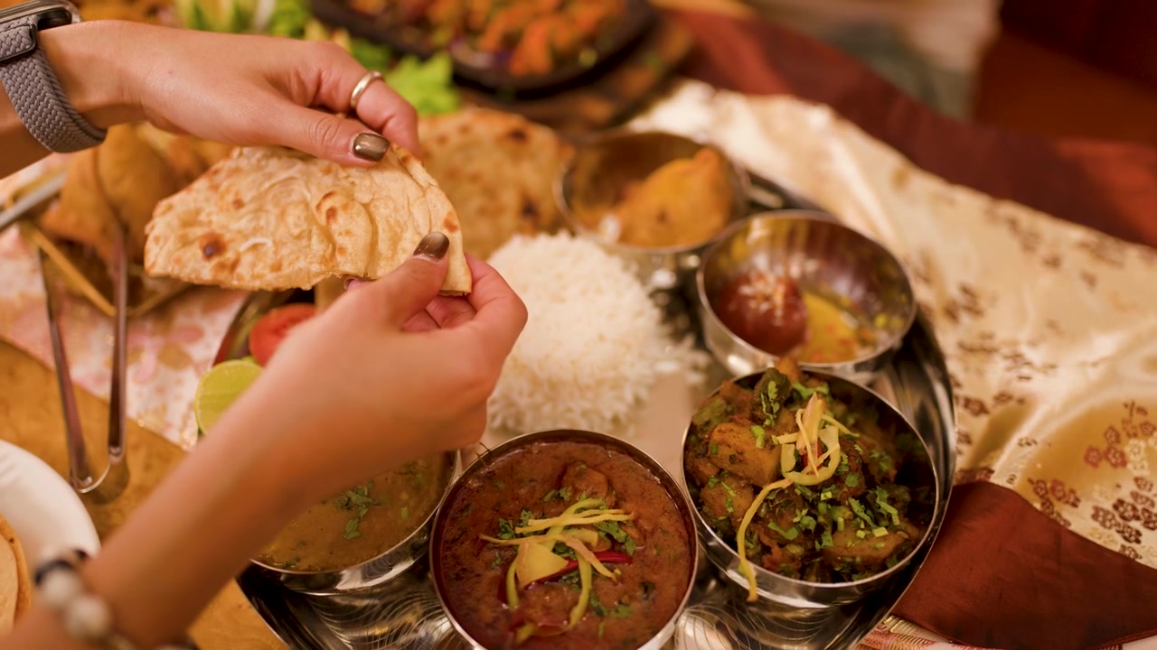 Primer plano de manos rompiendo pan plano sobre un thali indio diverso con curry y arroz