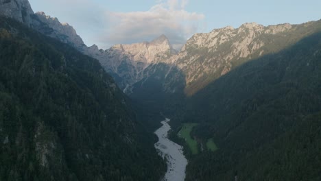 sunrise over robanov kot valley, with a river winding through forested mountains.
