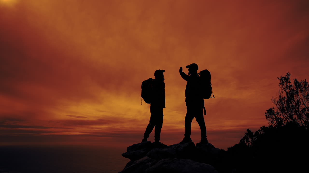 Two backpackers celebrating success on a mountain top at sunset