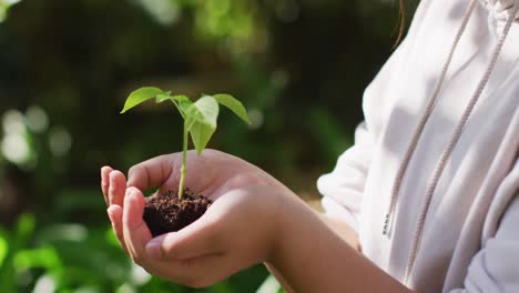 chica asiática sosteniendo una planta en el jardín en un día soleado
