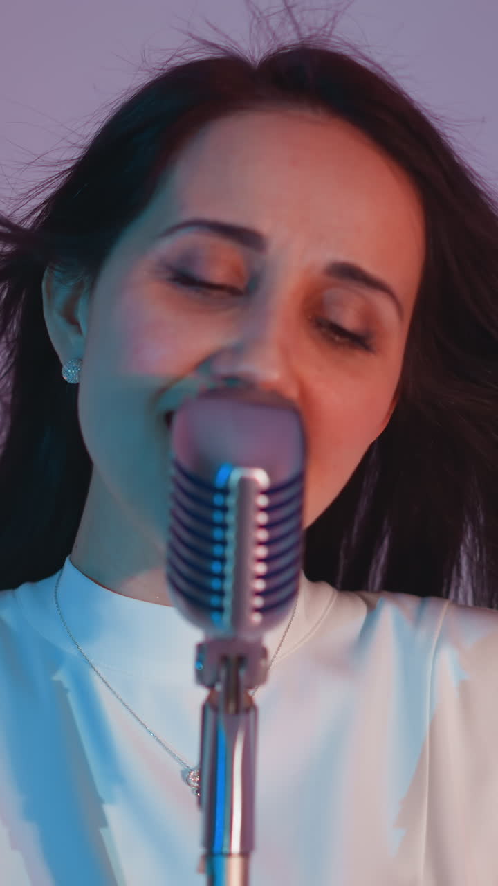 색 드레스를 입은 가수가 분홍색 배경에 머리카락이 부드럽게 흐르면서 열정적으로 노래하고 있습니다. 빈티지 마이크는 고전적인 터치를 추가합니다.