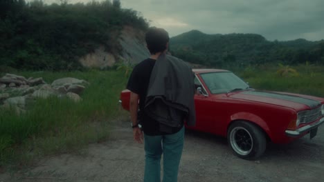 man walking towards a vintage red car in a mountainous landscape