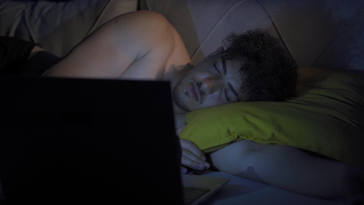 un joven somnoliento mirando su portátil. hora de dormir.