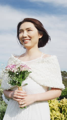 vertical video of happy asian bride holding bouquet and smiling at outdoor wedding