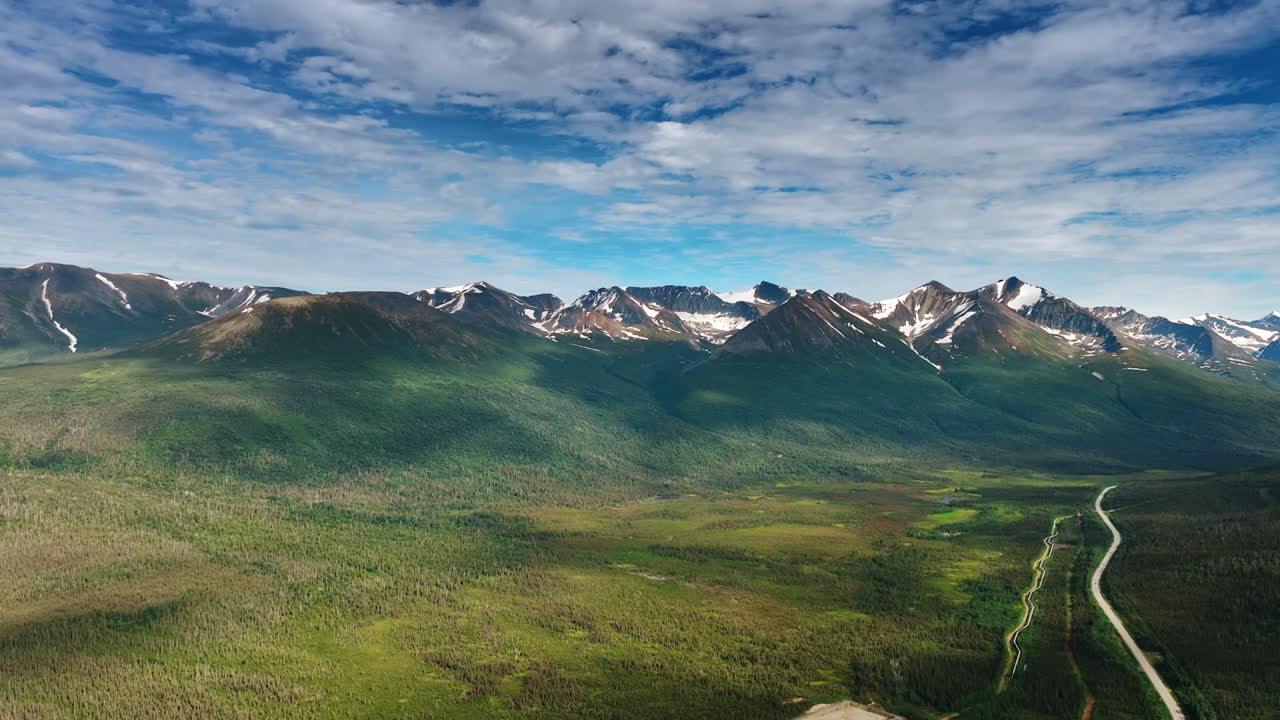 Iconic scenery of amazing mountains shaded by the clouds. A valley at the mountain foot crossed by the highway. Alaska, USA. Aerial view