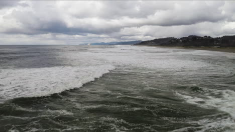 flying over ocean foamy waves along shore at neskowin beach with cloudy sky, oregon coast, aerial low altitude