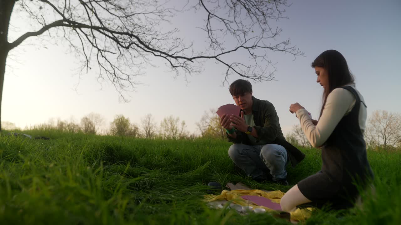 Friends playing cards in a park at sunset