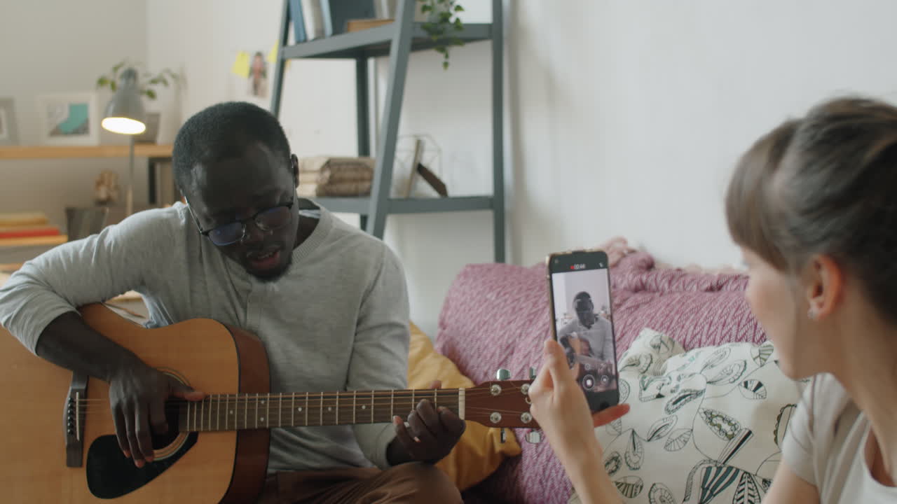 Uomo di colore che suona la chitarra e canta mentre la moglie filma un video