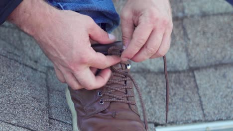 closeup of roof worker leg foot and hands tying laces on his work boot