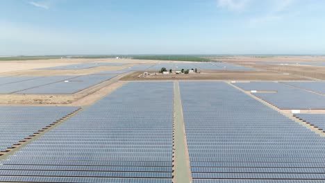 vertical rising tilt of a field covered in solar panels with some vineyards visible in the far distance during this warm afternoon