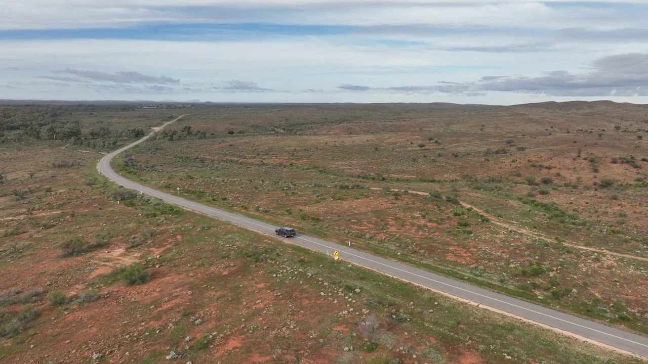 Ripresa aerea cinematografica in movimento che segue un veicolo lungo una strada tortuosa attraverso l'aspro entroterra di terra rossa vicino a Silverton e Broken Hill, Nuovo Galles del Sud