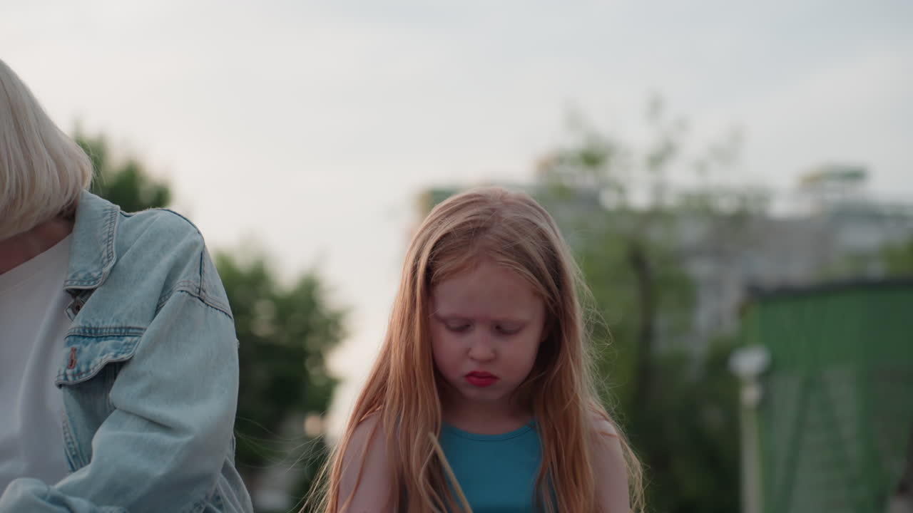 teenage girl holding pencil and paper drawing sketch on wooden dock as she blows paint residue off hands with distracted expression under soft sunset glow, capturing candid moment of creative pause