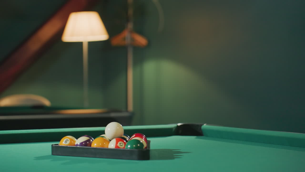 Vibrant billiard balls neatly arranged in triangle rack on green pool table in cozy billiard room with warm lighting. Classic cue sport setup highlighting white cue ball, and game atmosphere