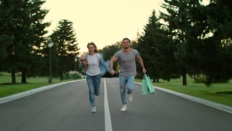 pareja feliz enamorada tomándose de las manos y corriendo por la carretera en el parque de verano